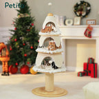 Three cats relaxing on different levels of a cream-colored, Christmas tree-themed cat tower placed in a cozy, decorated living room.
