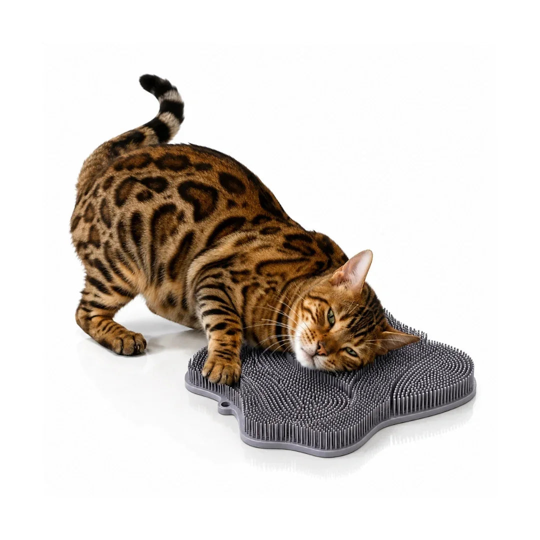 Bengal cat stretching and rubbing its head on a gray paw-shaped silicone cat self-groomer pad on the floor.